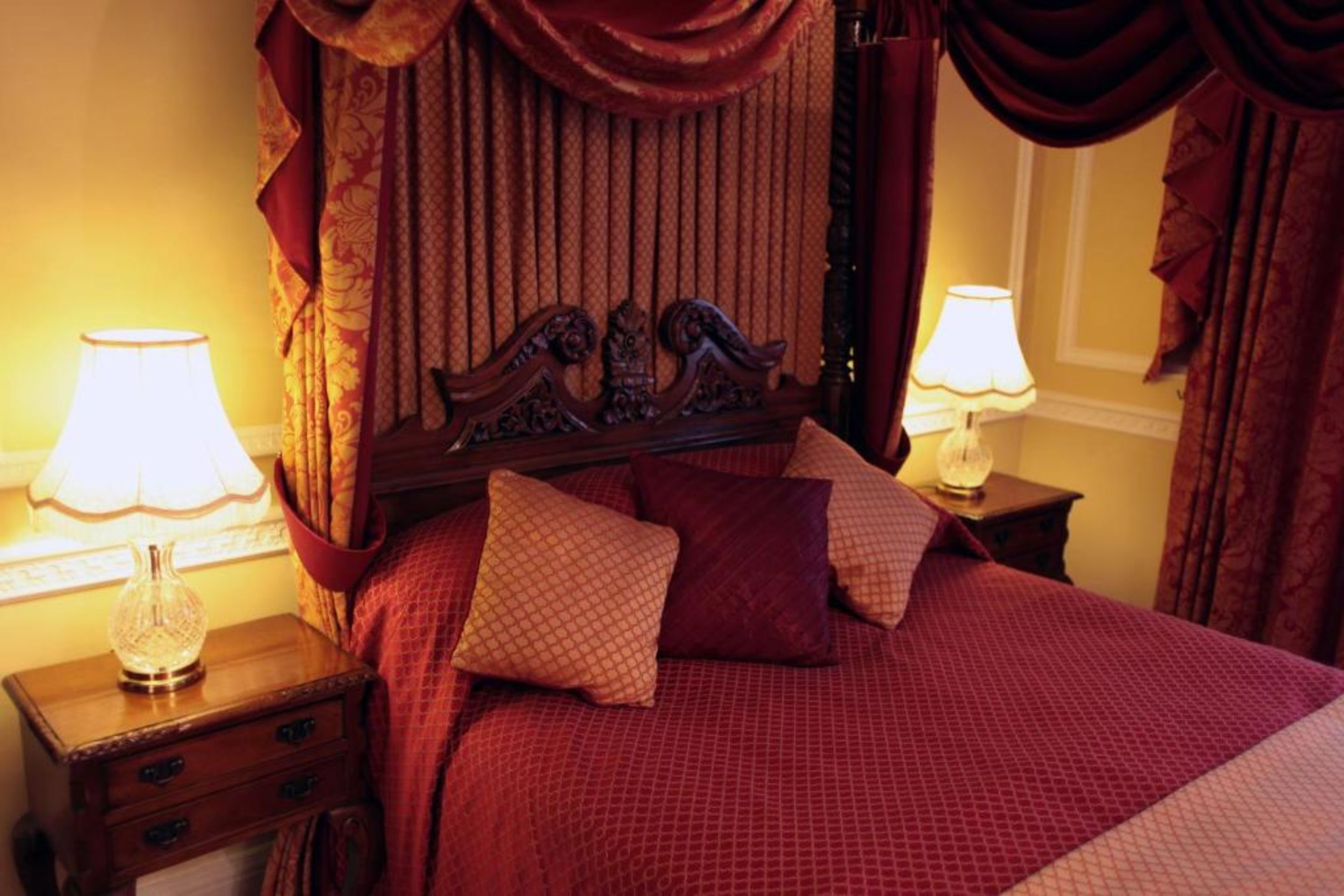Un dormitorio con cabecera de madera, dos mesitas de noche con lámparas y una colcha roja estampada.