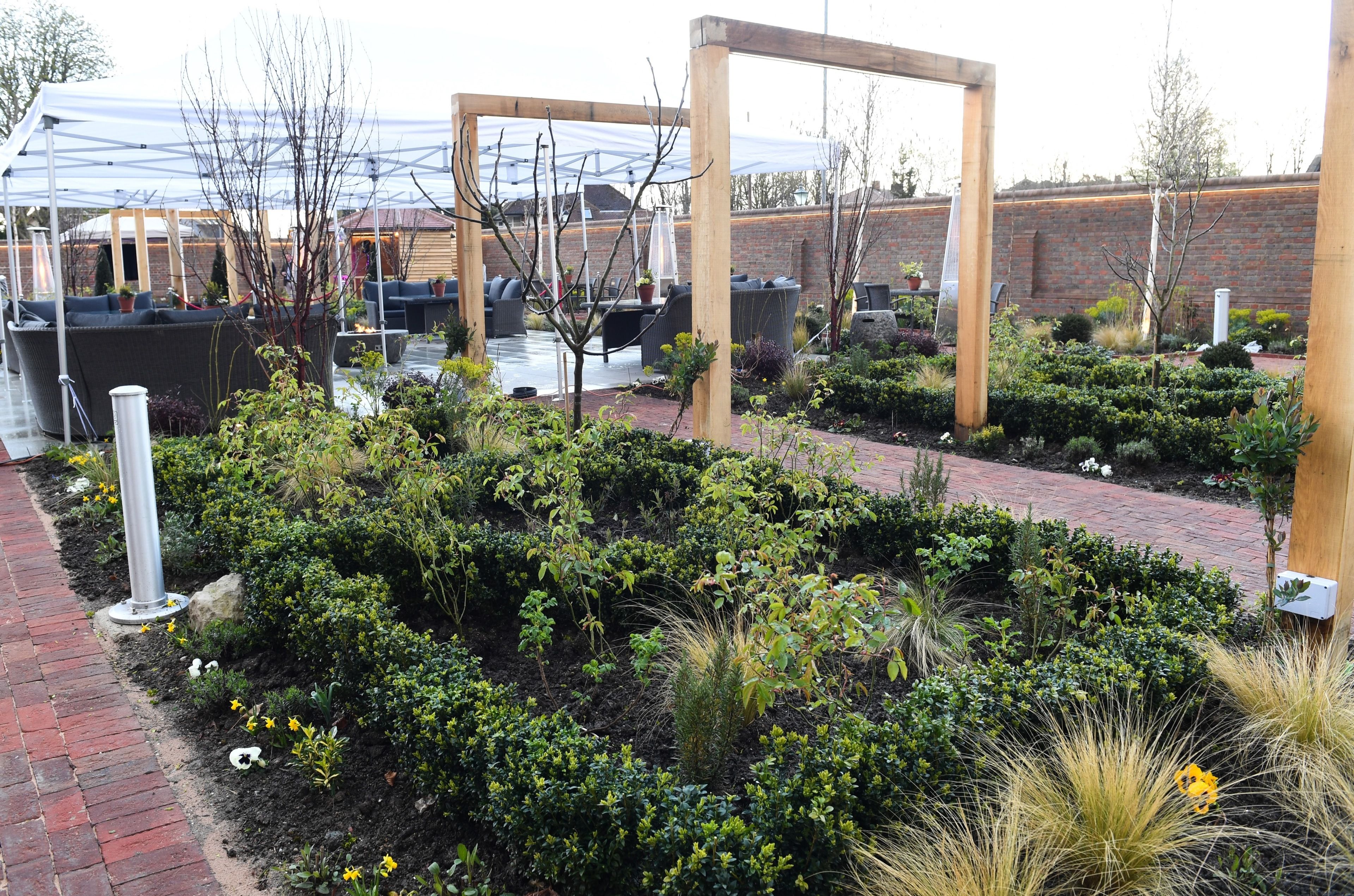 A garden area with a brick pathway, wooden pergola, and outdoor seating with cushions.