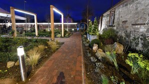Un sendero bien iluminado conduce a un edificio de fachada rústica, rodeado de jardines ajardinados y zonas de estar al aire libre.