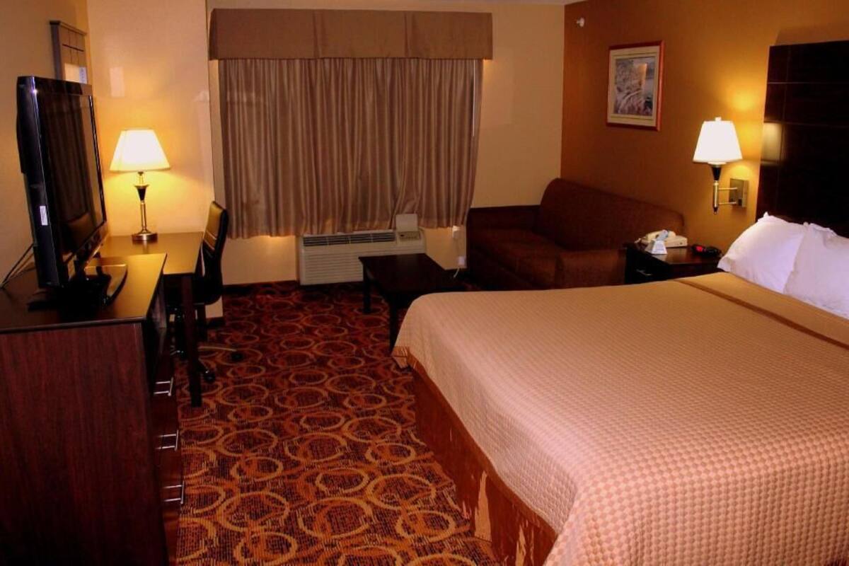 Ein Hotelzimmer mit Bett, Schreibtisch mit Lampe, Fernseher, Sofa und Wandlampe.
