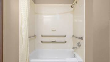 A bathroom with a bathtub, handrails, a towel, and a soap dispenser.