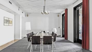 Une salle de conférence avec une longue table, des chaises, un lustre et de grandes fenêtres dotées de rideaux.