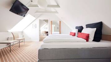 Una habitación de hotel moderna con una cama grande, un escritorio y un televisor montado en el techo.