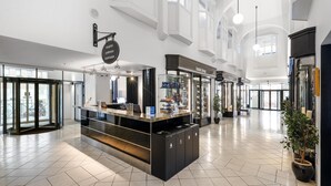 Un vestíbulo de hotel con mostrador de recepción, una tienda del hotel y una planta grande en maceta.