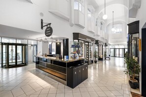 Un vestíbulo de hotel con mostrador de recepción, una tienda del hotel y una planta grande en maceta.