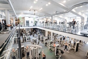 Un gimnasio de varios niveles con diferentes máquinas de ejercicio, una escalera central y barandilla de vidrio.