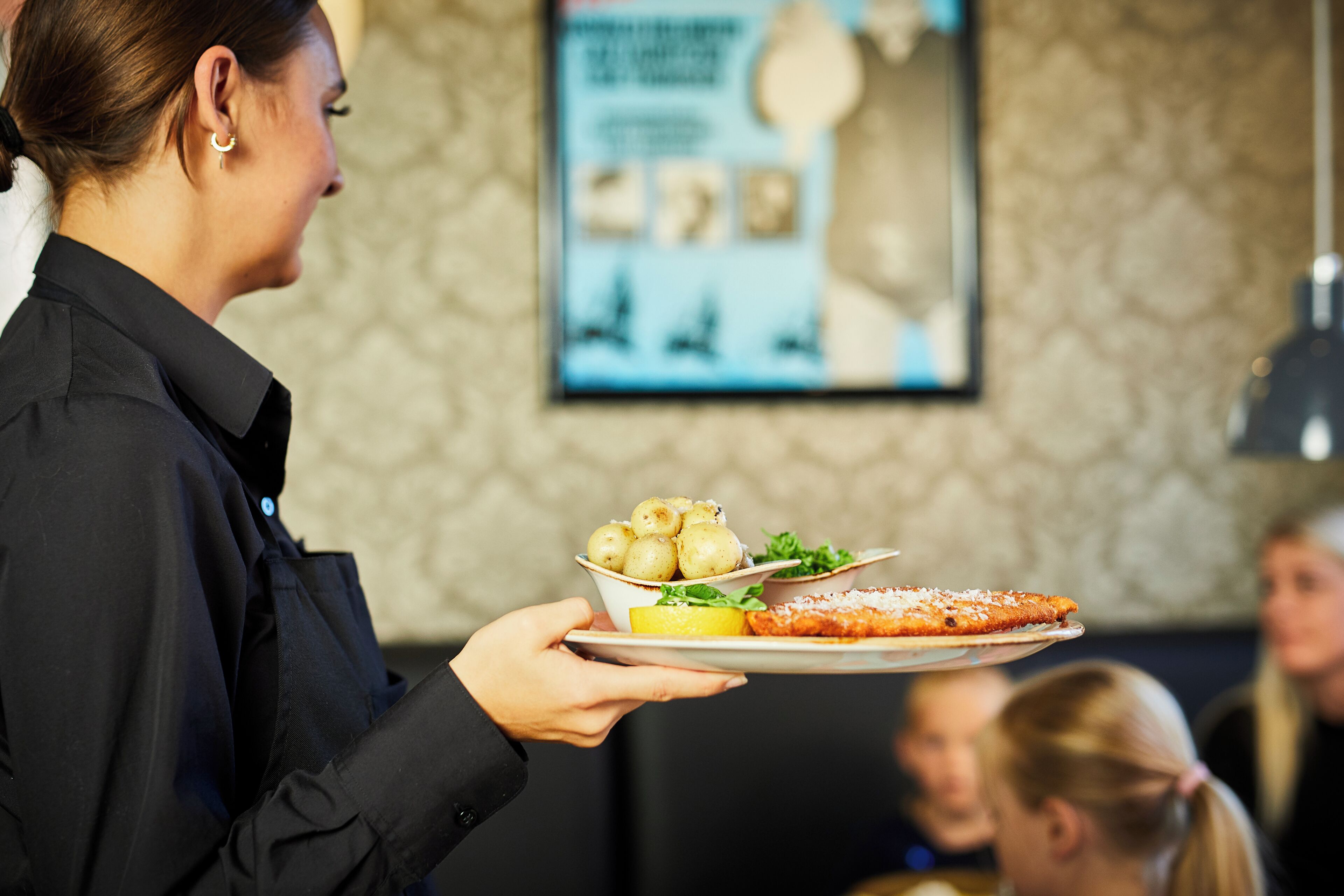 Iemand houdt een bord vast met eten, waaronder een stuk pizza, aardappelen en een partje citroen.