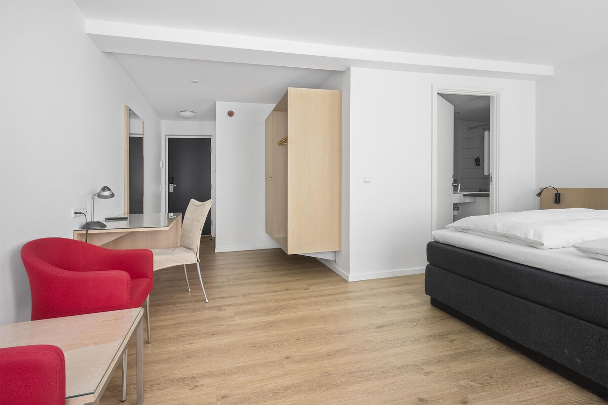Una habitación de hotel moderna con cama, escritorio, silla y armario.
