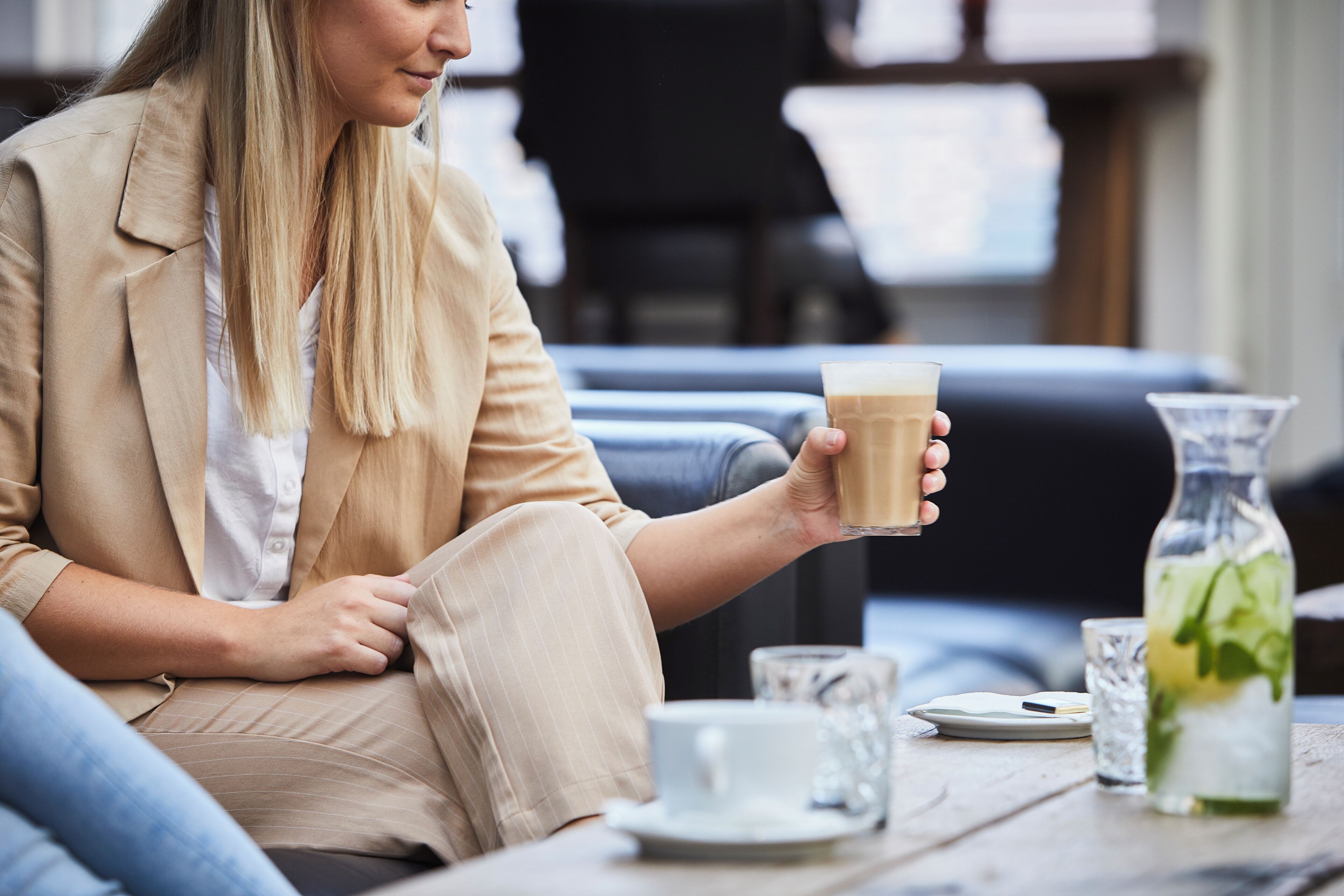 A person seated at a table with a glass of coffee, a glass of water, and a bottle of iced tea.