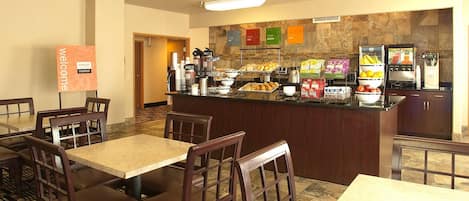 A breakfast area with tables and chairs, a counter with food items, and a 'Welcome' sign.