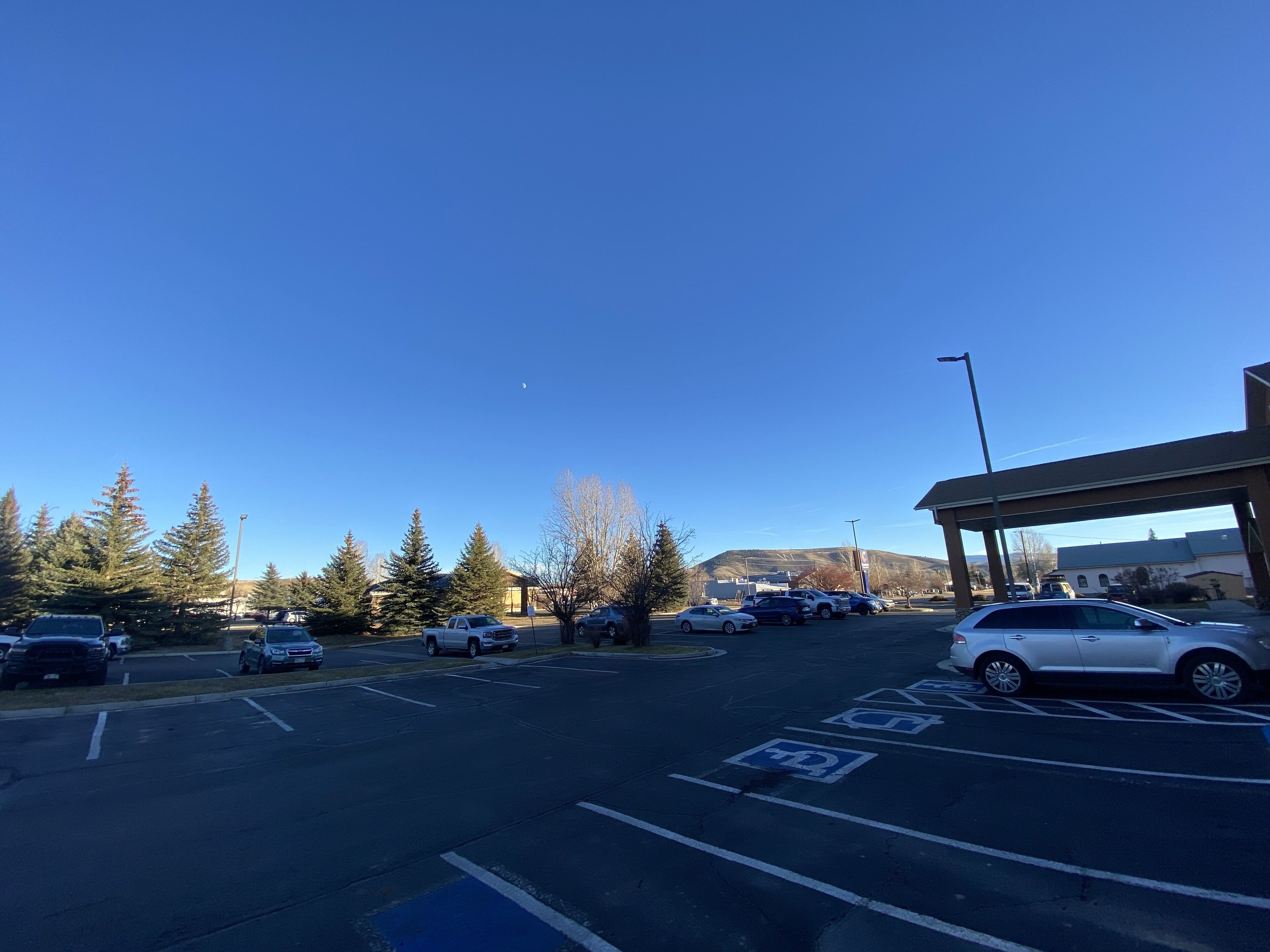 A parking lot with marked handicapped spaces, a covered area, and a clear sky.