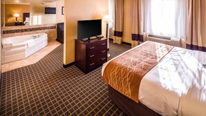 Hotelkamer met een groot bed, een flatscreen-tv, een badkuip, een bureau met lamp en een raam met gordijnen.