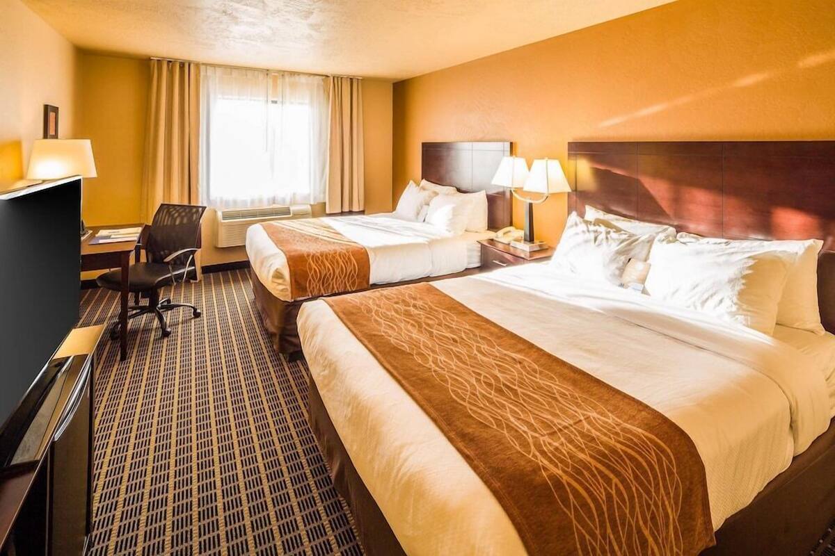 Habitación de hotel con dos camas, un escritorio, una silla y una ventana con cortinas.