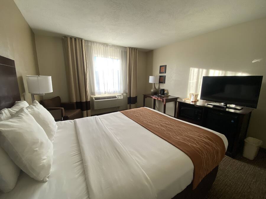 A hotel room with a large bed, a desk with a television, a lamp, and a window with curtains.