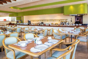 Un comedor amplio con múltiples mesas y sillas, una barra central y una cocina al fondo.