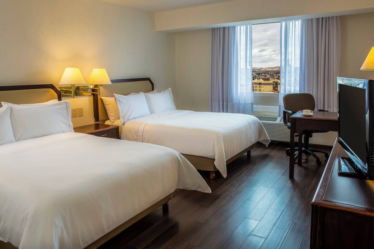 A hotel room with two beds, a desk, a chair, and a TV.