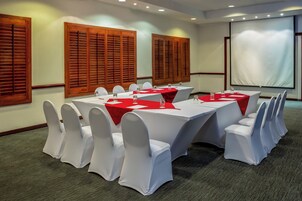 Una sala de conferencias con una larga mesa, sillas blancas y una pantalla para proyector.