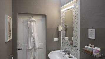 Un bagno con un lavandino bianco, uno scaffale in vetro con articoli da toilette, uno specchio e un asciugamano appeso alla porta.