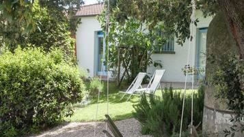A wooden swing set in a garden with a white building in the background.