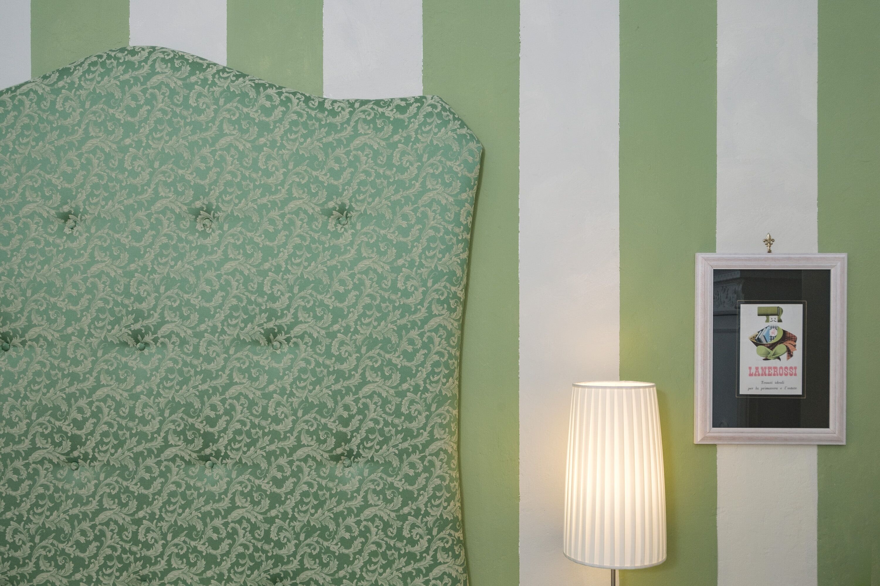 A room with a green and white striped wall, a patterned headboard, and a framed picture on the wall.