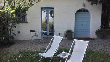 Een wit gebouw met een blauwe deur en een raam, twee witte lounge stoelen en een kleine tafel met een lantaarn.