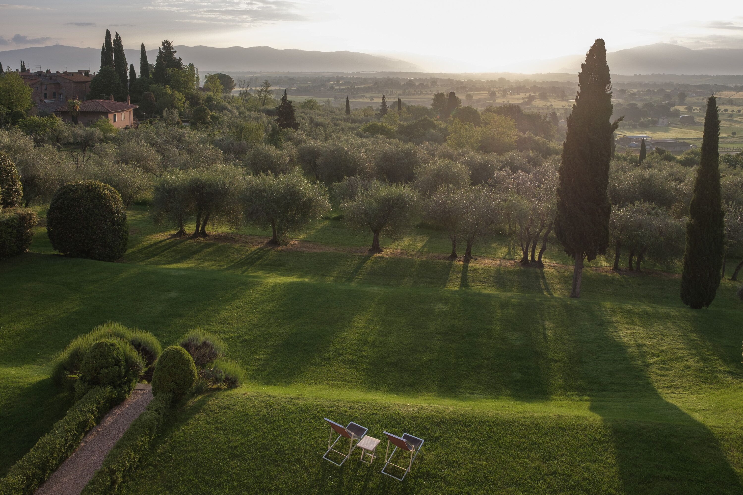 A lush garden with neatly trimmed hedges, a pathway, and two chairs.