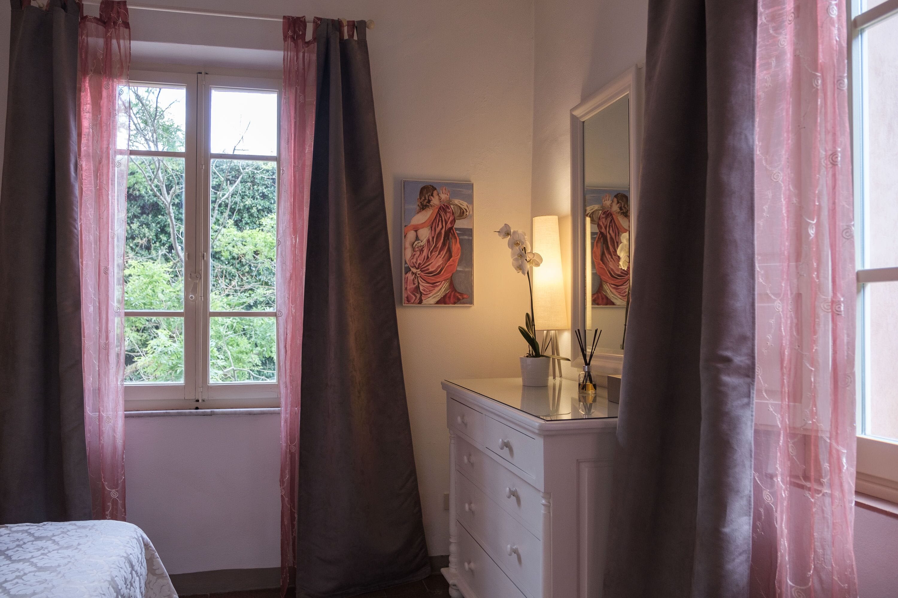 A bedroom with a bed, a dresser, a mirror, and a window with curtains.