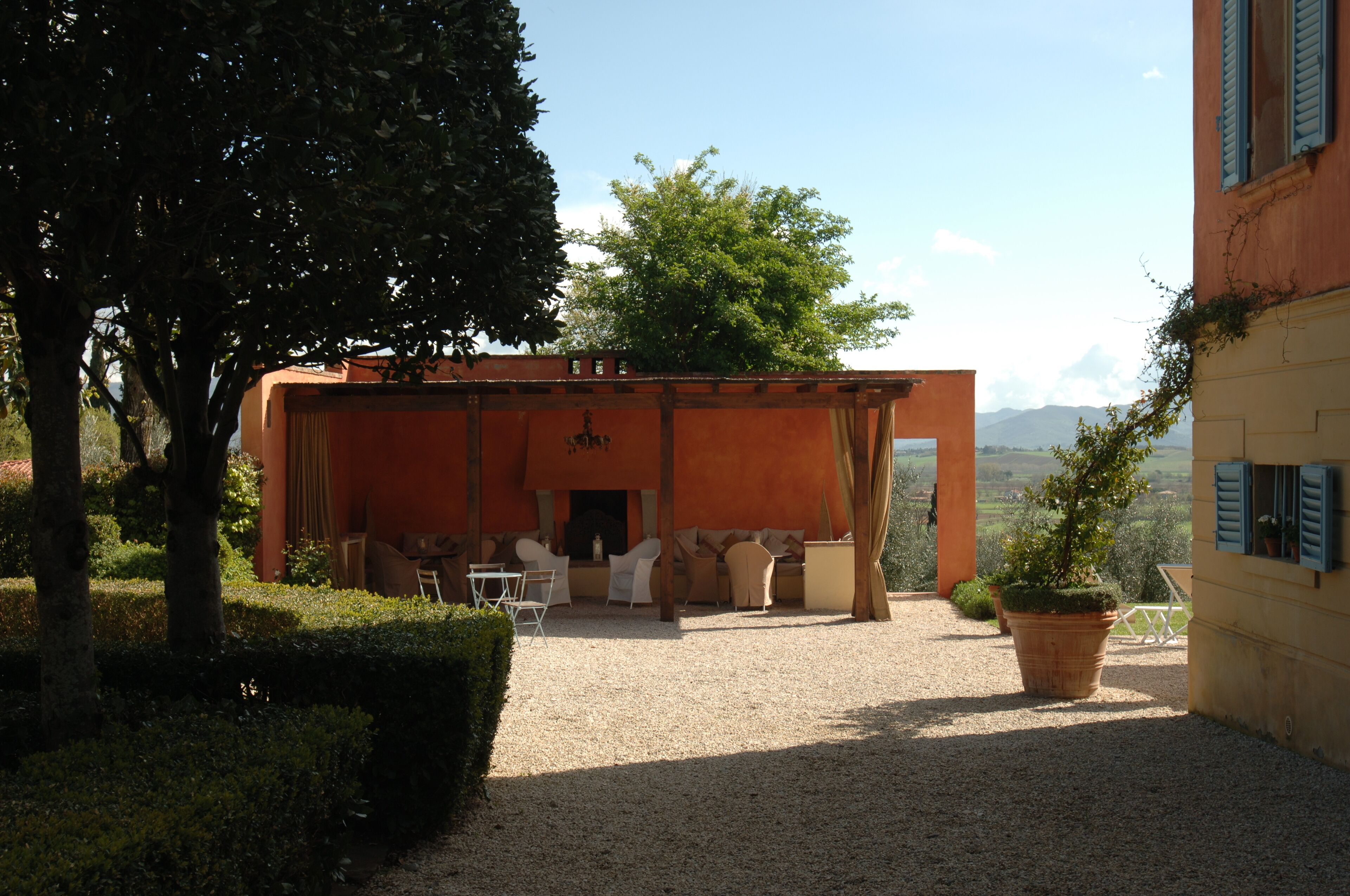 An outdoor seating area with a fire pit, surrounded by a gravel patio and a hedge.