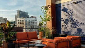 Eine Dachterrasse mit orangefarbenen Sitzgelegenheiten, einem kleinen Tisch und Blumentöpfen.