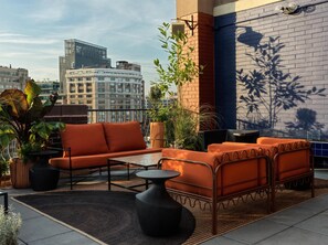 A rooftop terrace with orange seating, a small table, and potted plants. - The Manner, The Unbound Collection by Hyatt (New York)