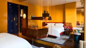 Une chambre d’hôtel avec un grand miroir, un lit, un bureau et une chaise rouge.