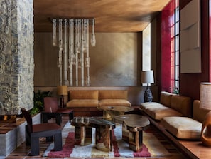 A modern living room with a sofa, coffee table, and chairs, a hanging light fixture, and a large window. - The Manner, The Unbound Collection by Hyatt (New York)