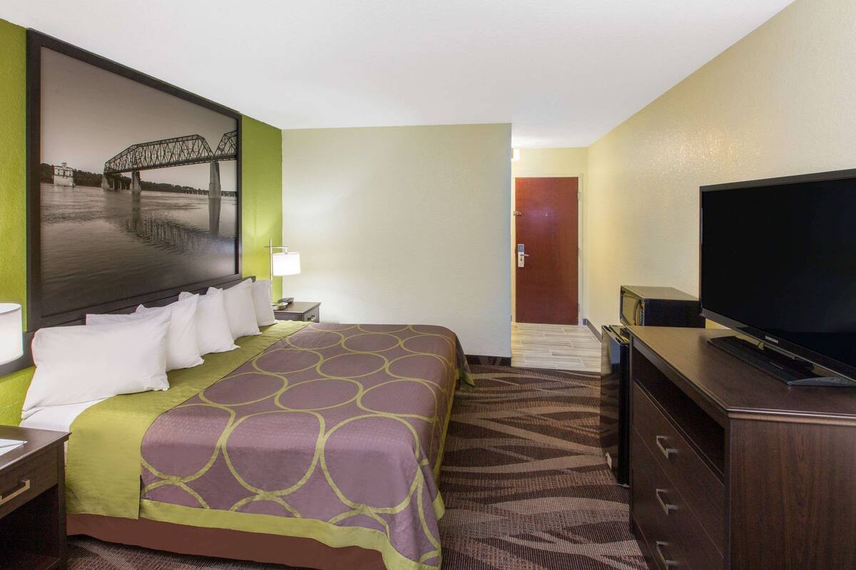 Une chambre d’hôtel avec un grand lit, un téléviseur à écran plat, une commode et un tableau représentant un pont.