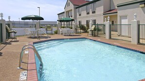 A swimming pool with a metal ladder, surrounded by white lounge chairs and green umbrellas.