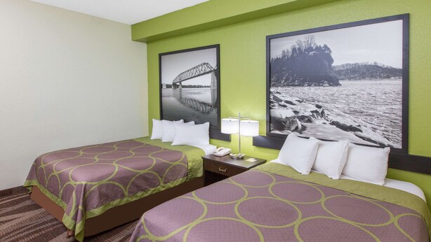 A hotel room with two beds, each with a patterned bedspread, a nightstand with a lamp, and two framed pictures on the wall.