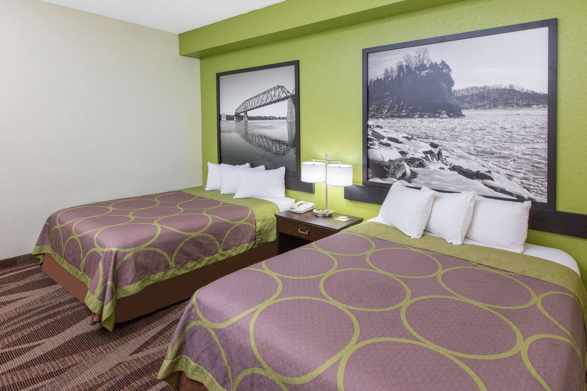 Une chambre d’hôtel avec deux lits, chacun recouvert d’une couvre-lit à motifs, une table de chevet avec une lampe et deux tableaux encadrés accrochés au mur.