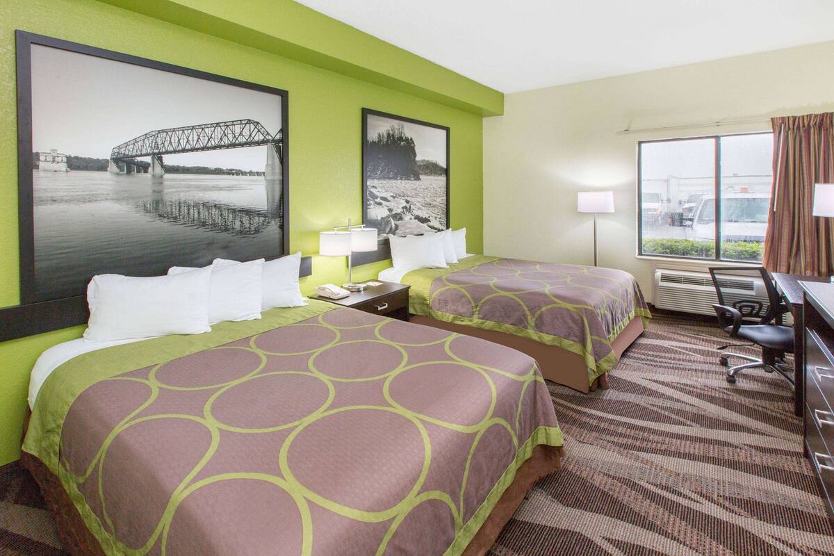Une chambre d’hôtel avec deux lits, un bureau, une chaise et une fenêtre donnant sur un pont et sur l’eau.