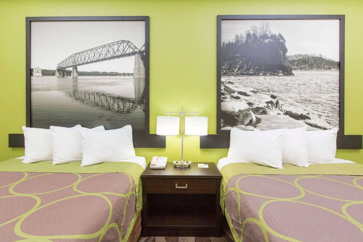 Une chambre d’hôtel avec deux lits, une table de chevet, une lampe et deux tableaux encadrés au mur.