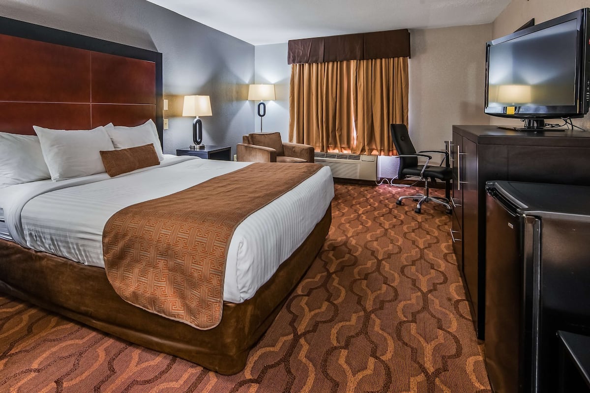A hotel room with a large bed, two bedside lamps, a TV, a desk, and a chair.