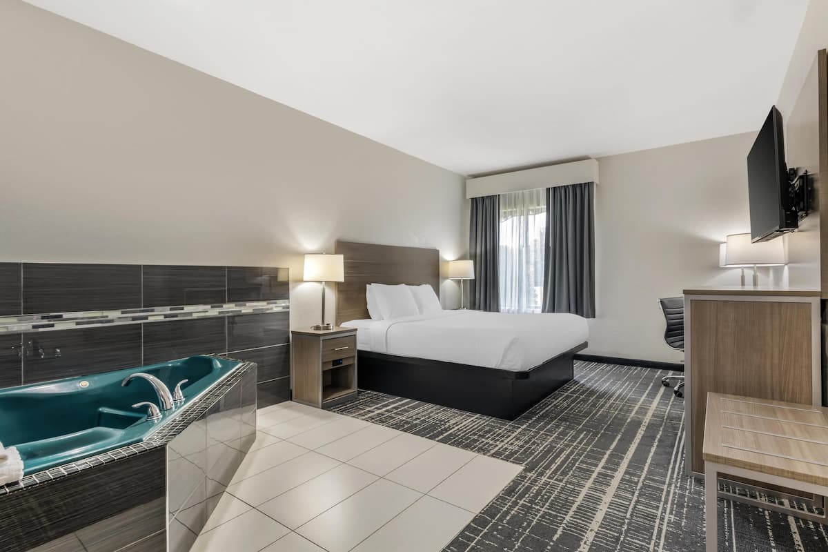 A hotel room with a large bed, a bathtub, a desk, and a TV.