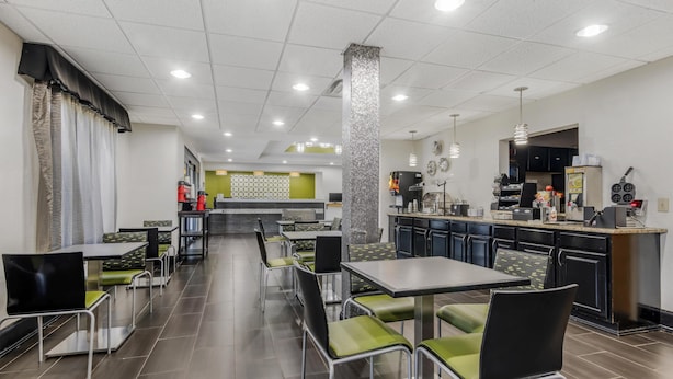 Un restaurante moderno con una larga barra, sillas con cojines verdes y una zona de cocina con una cafetera y un tablero de menú.