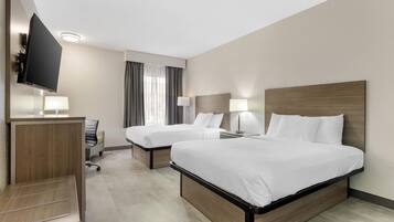 A hotel room with two beds, a desk, a TV, and a chair.