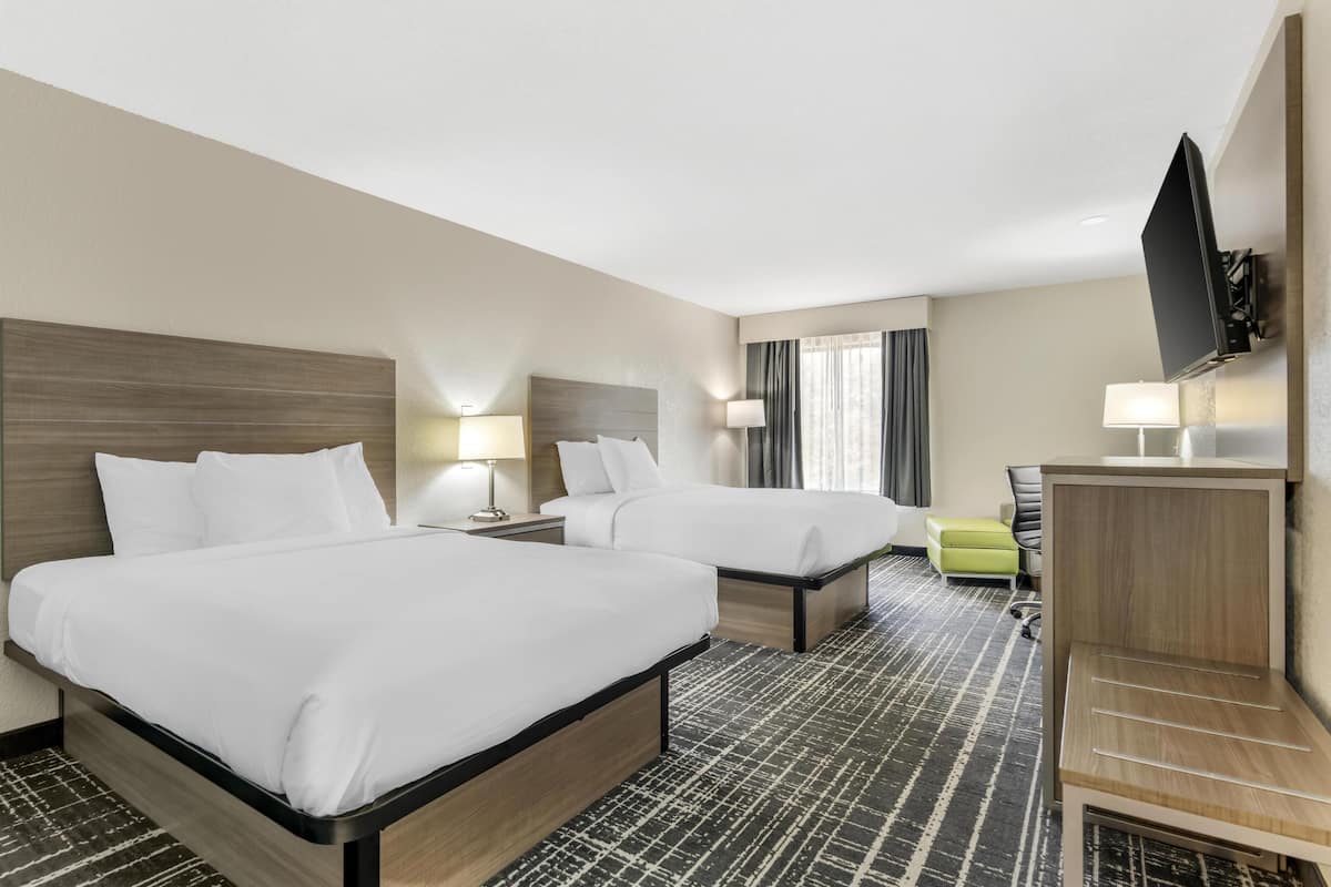 A hotel room with two beds, a desk, a TV, and a window with curtains.