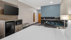Habitación de hotel con cama, televisor de pantalla plana en la pared, refrigerador, microondas, una mesita y baño con bañera y lavamanos.