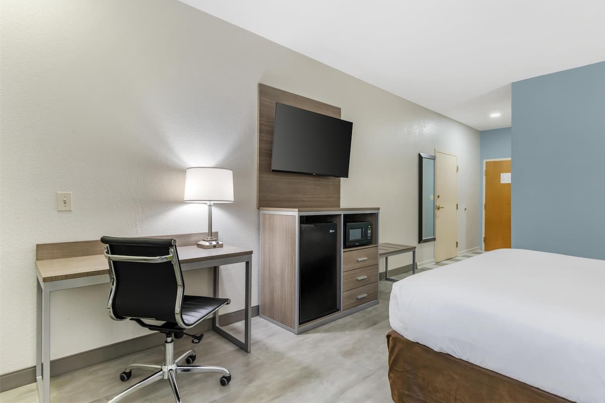 A hotel room with a bed, desk, chair, microwave, and TV.