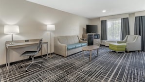 Una habitación de hotel con escritorio, sofá, sillón, televisor y una pequeña mesa.