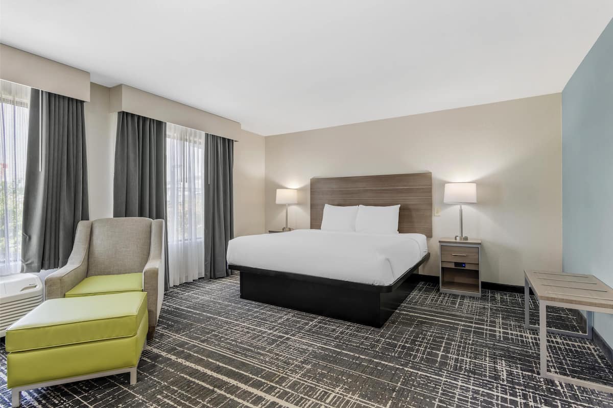 A hotel room with a large bed, a chair, a desk, and a lamp.