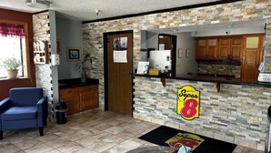 A lobby with a reception desk, a blue chair, a trash bin, a potted plant, and a wall-mounted sign. - Super 8 by Wyndham Boone (Boone)