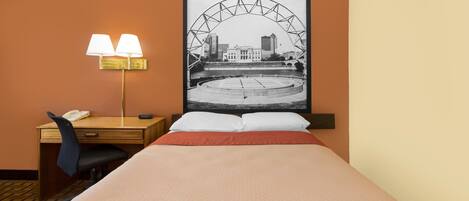 Una habitación de hotel con una cama, un escritorio con lámpara y una imagen enmarco de un paisaje urbano.