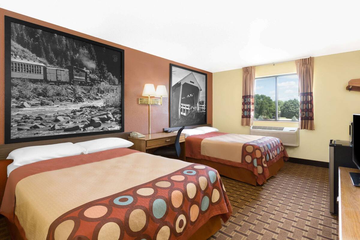 A hotel room with two beds, a desk, a chair, a television, and two framed pictures on the wall.